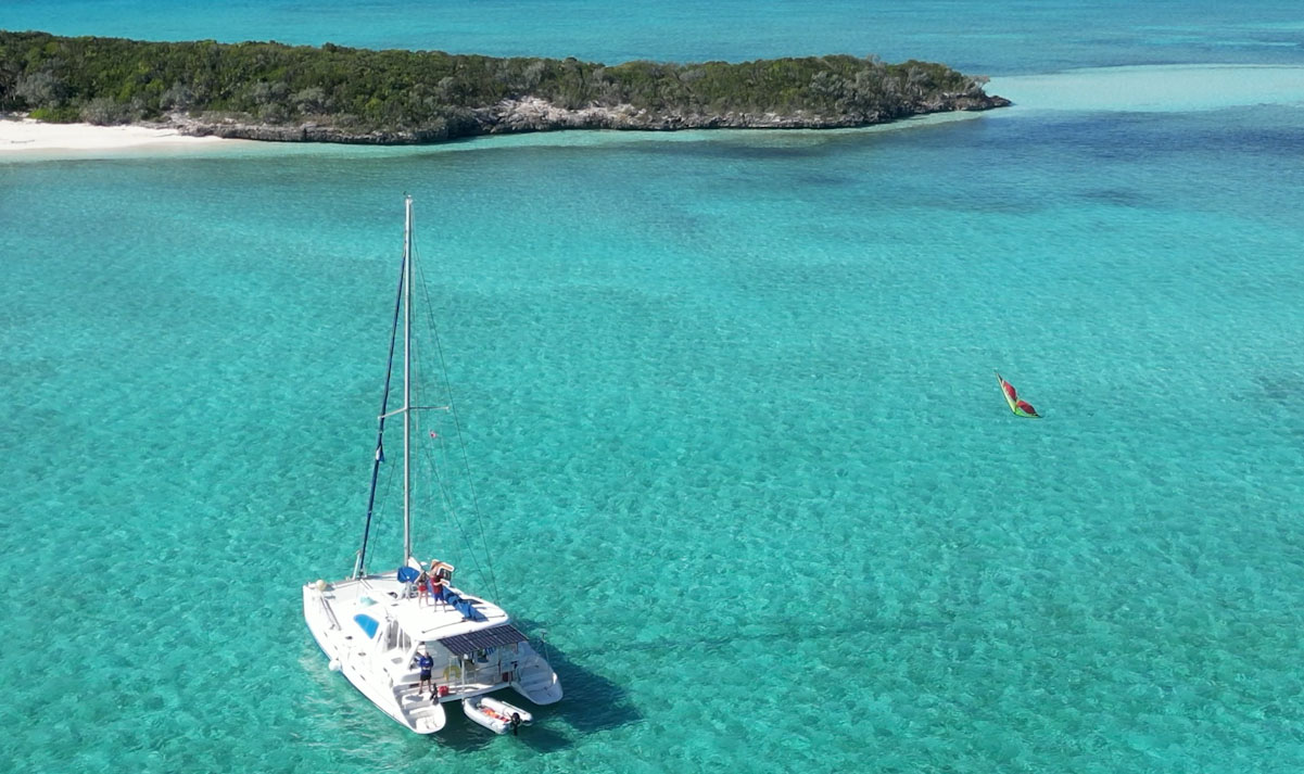 Bon Bida catamaran anchored in pristine turquoise waters with an uninhabited island in the background, showcasing the remote and private experience of catamaran cruising versus crowded resort beaches